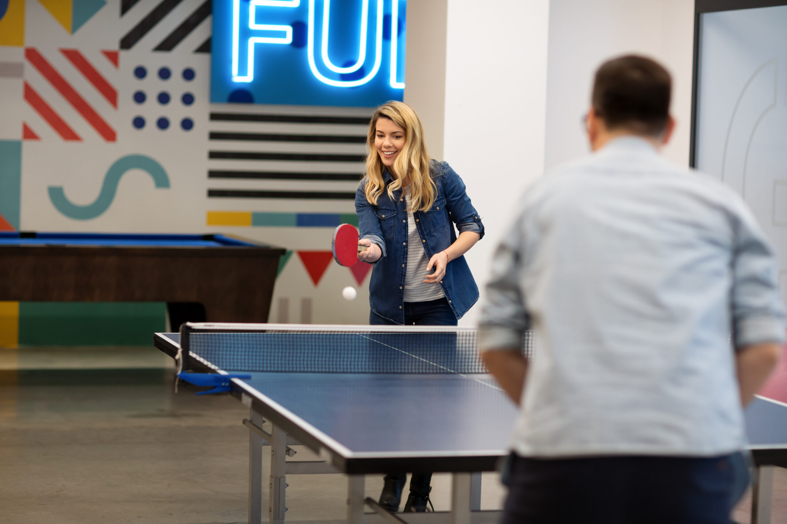 Young woman playing table tennis with her colleague